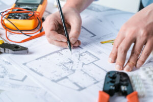 Man repairer making electricity project in house.Repairs planning.Drawing,diagrams,plan of electrification of apartment,building.Devices,accessories,voltmeter,wires,screwdriver,pliers and tape measure